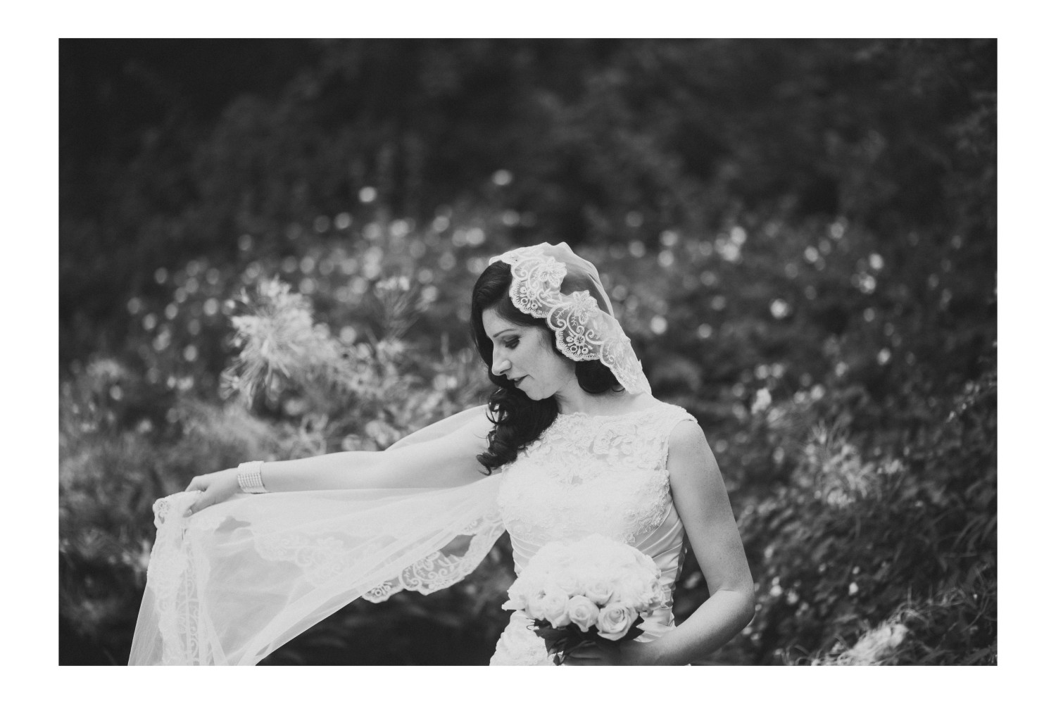 Black and white portrait of the bride swinging her lace veil during wedding portraits.