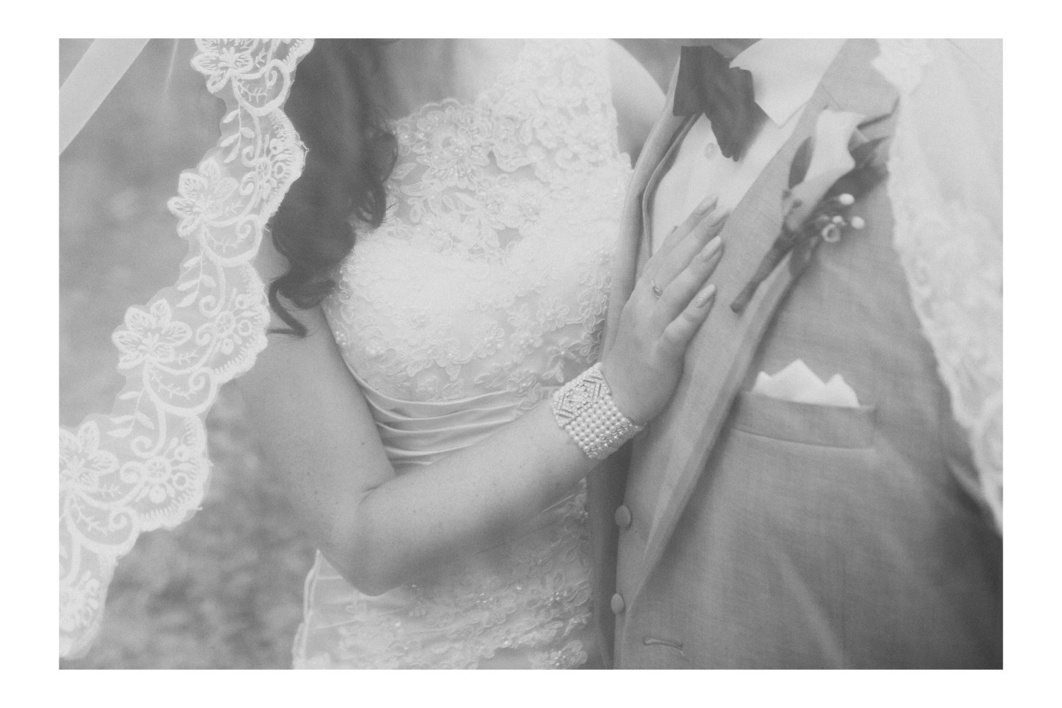 Black and white wedding portrait of the bride and groom hugging under the veil.
