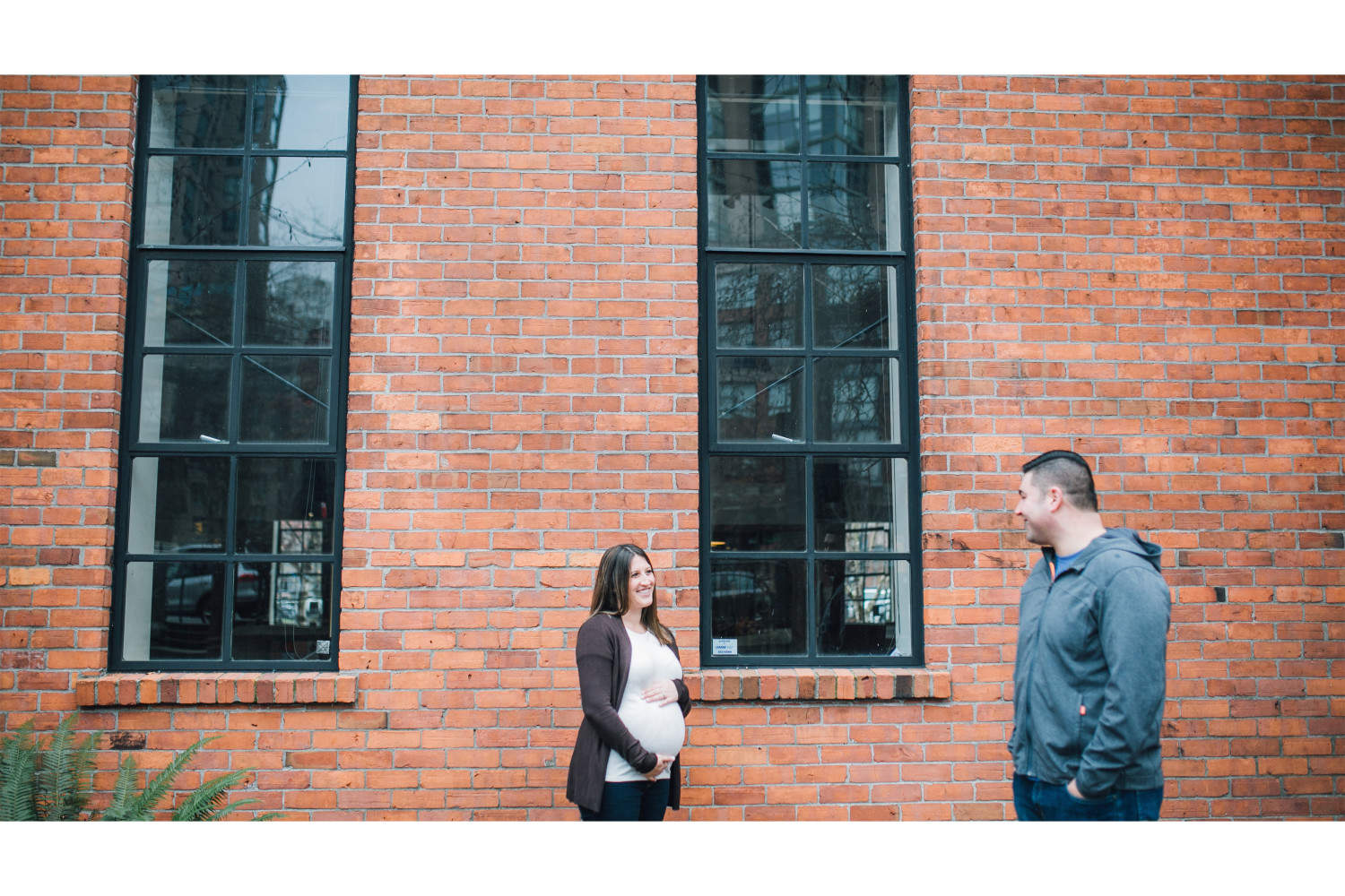Couple standing in front of brick wall during Vancouver maternity session.